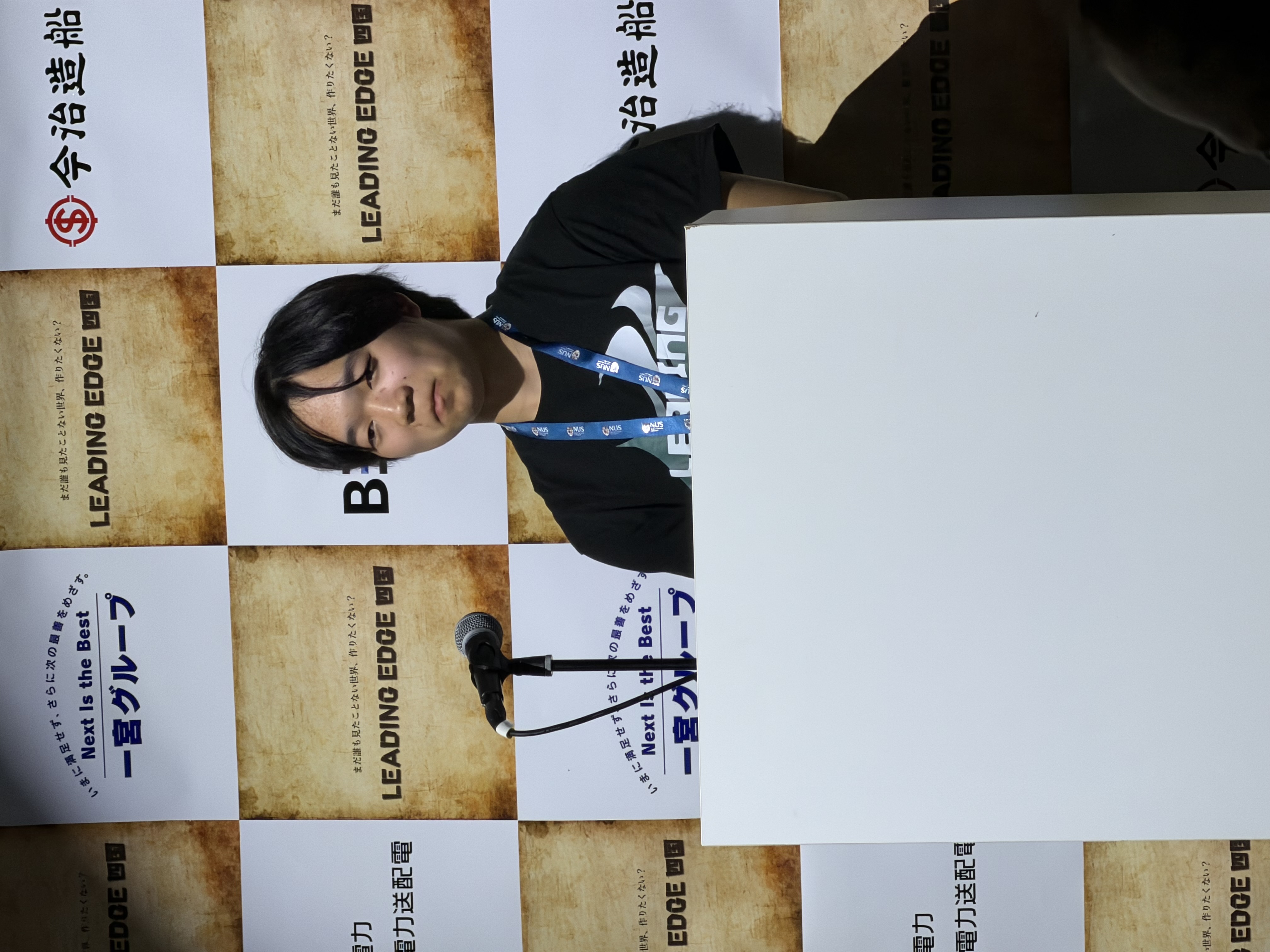 シンガポール国立大学（NUS）のストラップを首にかけ、ピッチイベントの演台で登壇する奥河董馬